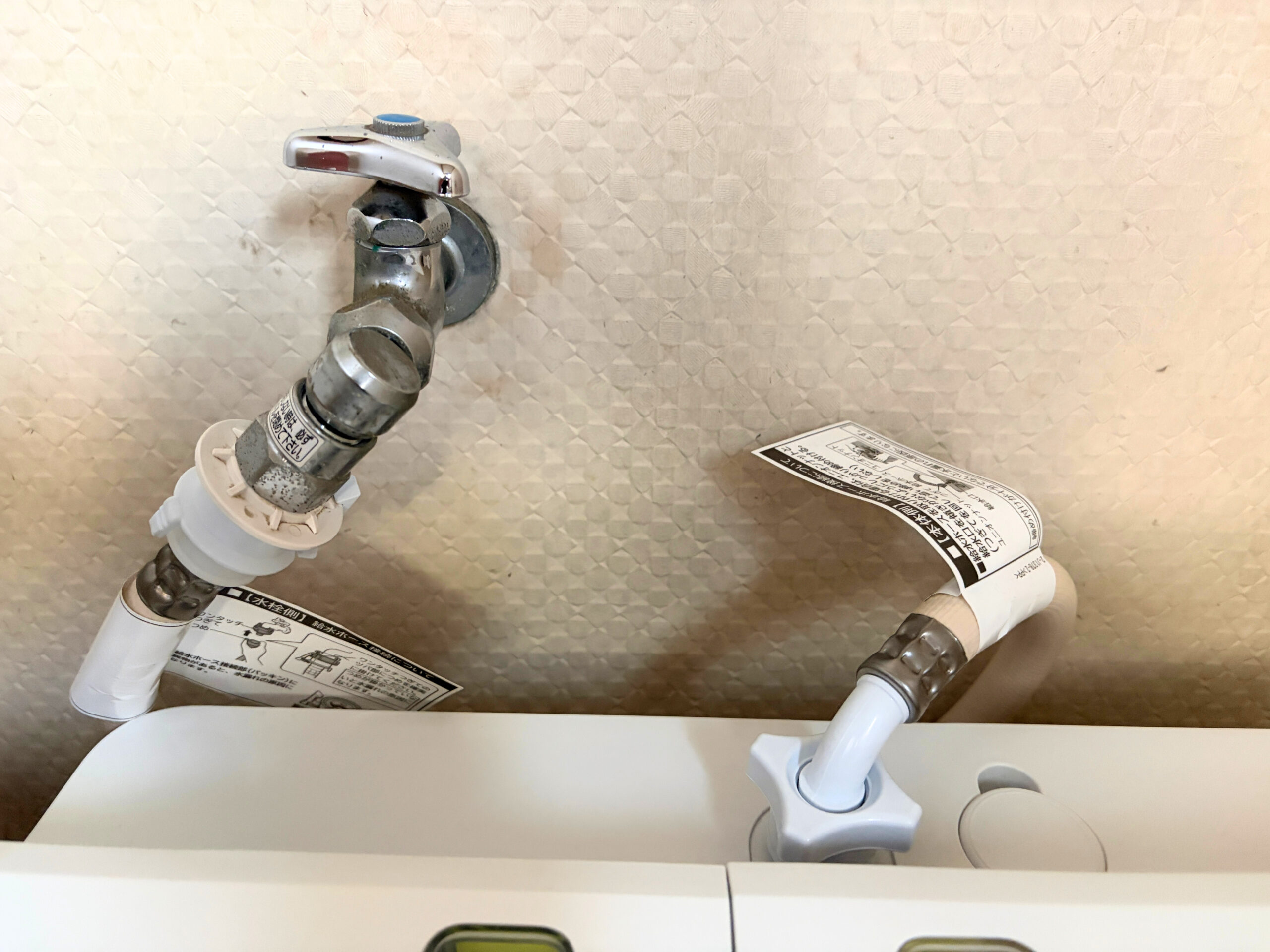 洗濯機の背面上部を上から撮影し 給水ホースの蛇口側と本体側の接続部分を一緒に写した写真